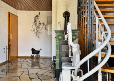 Eingangsbereich im Erdgeschoss mit gefliestem Boden, Zugang zu den Wohnräumen und kleinem, nicht angeschlossenem Kamin. Ein Treppenlift ist auch vorhanden.