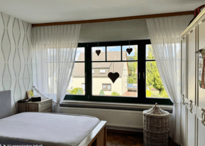 Schlafzimmer im Obergeschoss mit großer Fensterfront zur Vorderseite – heller Raum mit viel Tageslicht